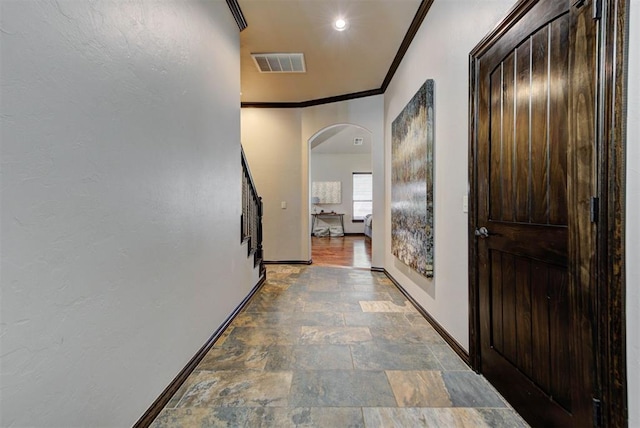 hallway with arched walkways, visible vents, ornamental molding, stone finish floor, and baseboards