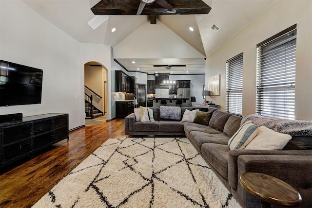 living area featuring arched walkways, high vaulted ceiling, wood finished floors, visible vents, and stairway