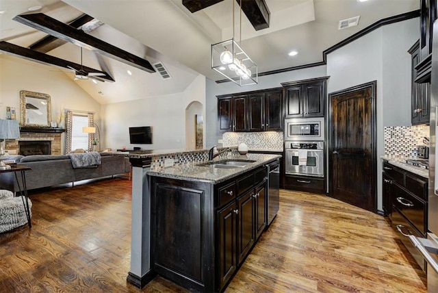 kitchen with arched walkways, a fireplace, a sink, visible vents, and appliances with stainless steel finishes