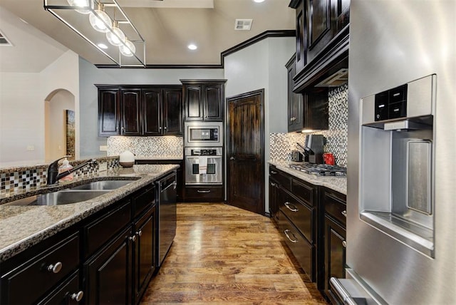 kitchen with light stone counters, light wood-style flooring, stainless steel appliances, a sink, and tasteful backsplash