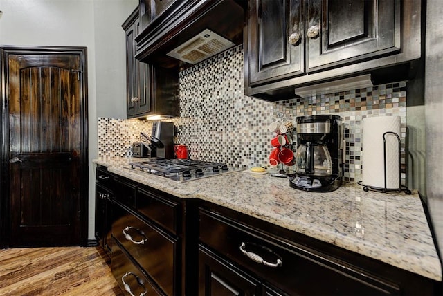 kitchen with light wood finished floors, light stone countertops, under cabinet range hood, stainless steel gas cooktop, and backsplash