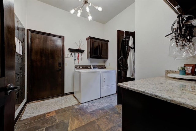 clothes washing area featuring stone finish floor, washing machine and dryer, cabinet space, and a notable chandelier