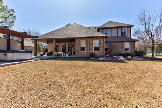 rear view of house featuring a patio, brick siding, a shingled roof, and a hot tub