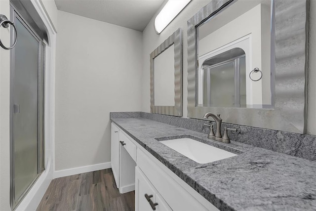 bathroom with a stall shower, vanity, baseboards, and wood finished floors