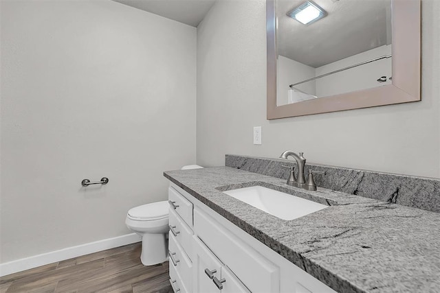 bathroom featuring toilet, baseboards, wood finished floors, and vanity