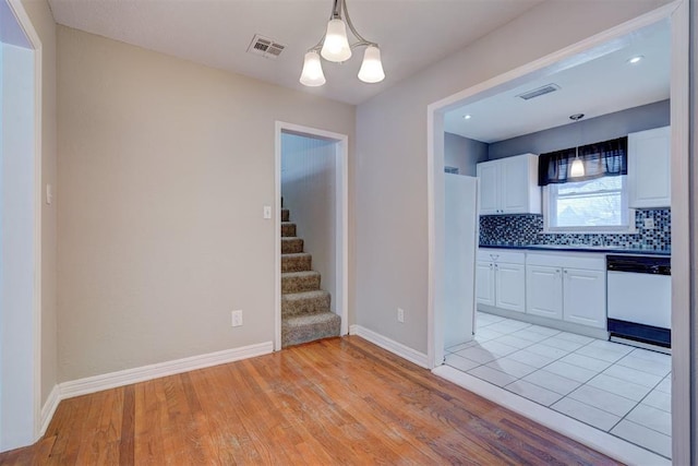 kitchen featuring white dishwasher, visible vents, white cabinets, and decorative backsplash