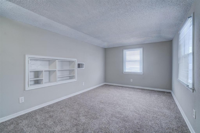 spare room with carpet, a textured ceiling, visible vents, and baseboards