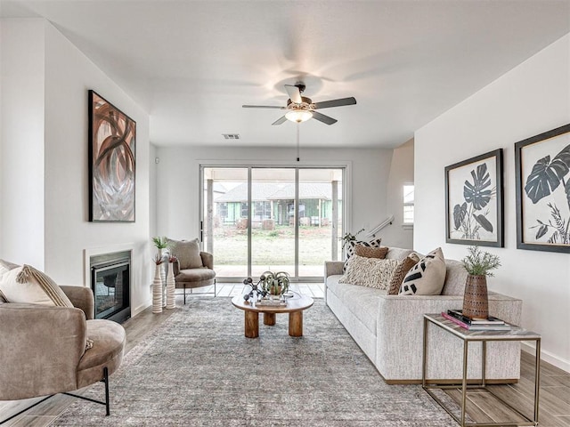 living room with a glass covered fireplace, wood finished floors, visible vents, and baseboards