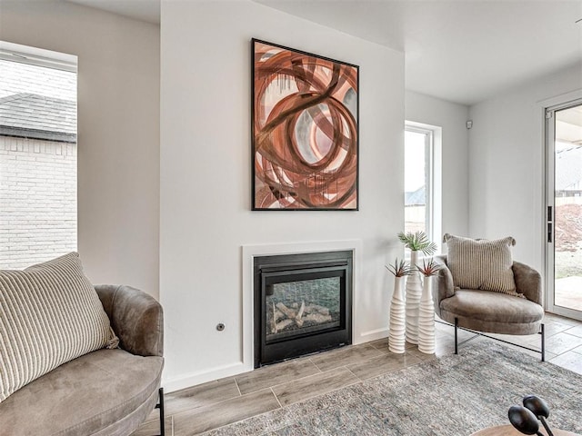 sitting room with baseboards, a glass covered fireplace, and wood tiled floor