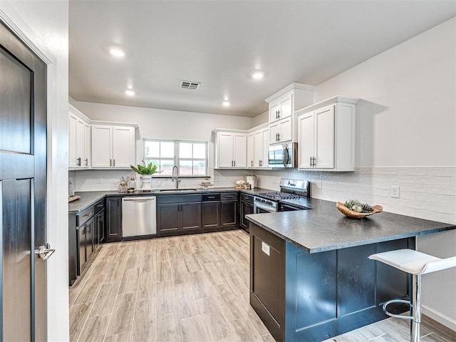 kitchen featuring visible vents, dark countertops, appliances with stainless steel finishes, a peninsula, and a sink