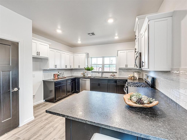 kitchen featuring a sink, visible vents, light wood-style floors, appliances with stainless steel finishes, and dark countertops