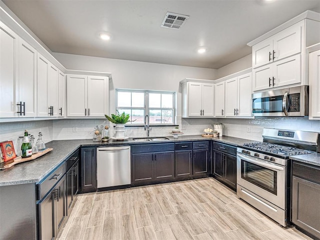 kitchen with visible vents, decorative backsplash, stainless steel appliances, white cabinetry, and a sink