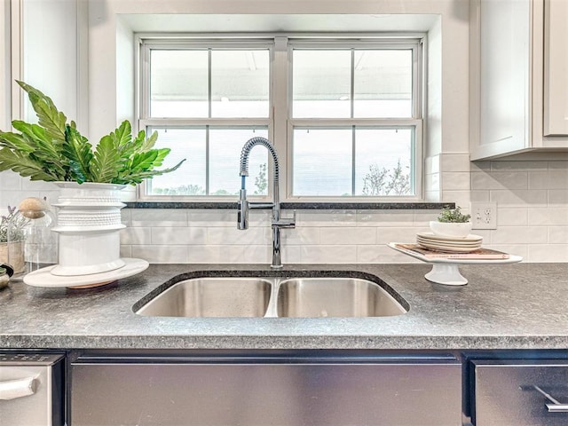 details featuring dark countertops, stainless steel dishwasher, tasteful backsplash, and a sink