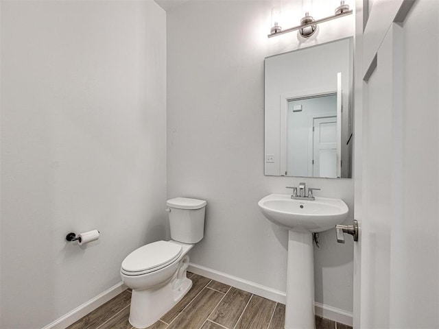 half bathroom with toilet, wood tiled floor, baseboards, and a sink