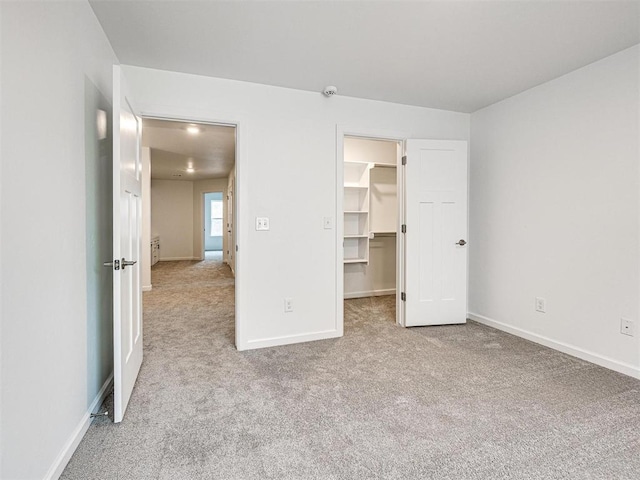 unfurnished bedroom with carpet floors, a closet, a spacious closet, and baseboards