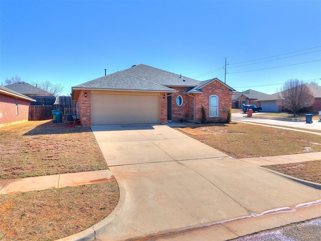 single story home with a garage, concrete driveway, roof with shingles, fence, and brick siding