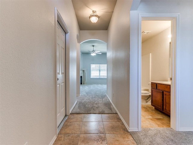 hallway with arched walkways, light tile patterned flooring, light colored carpet, visible vents, and baseboards