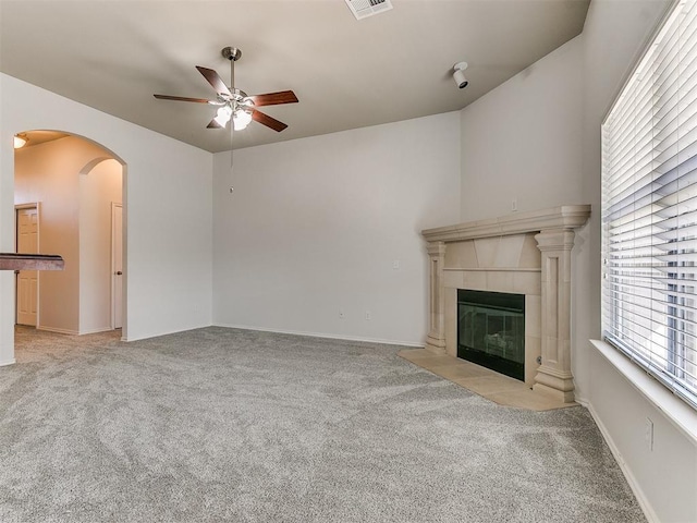 unfurnished living room featuring arched walkways, light carpet, ceiling fan, and a tiled fireplace