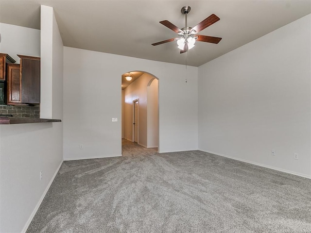 carpeted spare room with arched walkways, ceiling fan, and baseboards