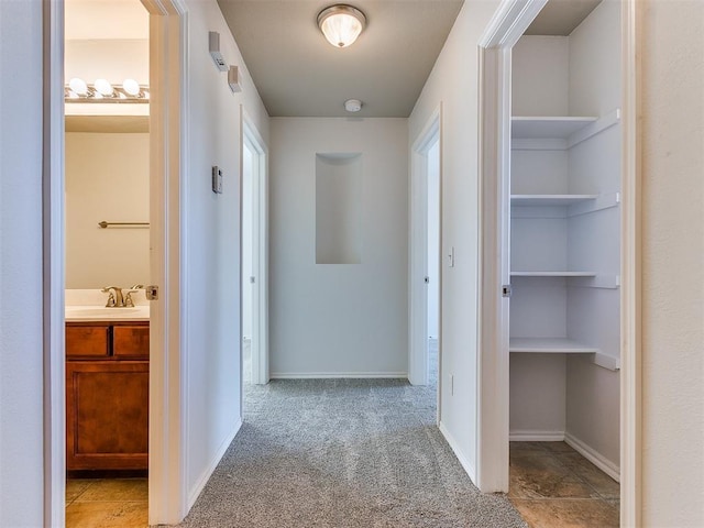 hall with a sink, baseboards, and carpet flooring