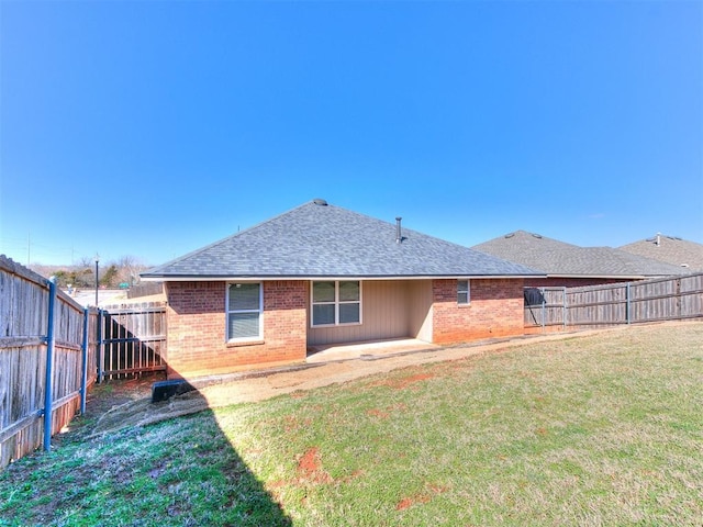 back of property with brick siding, a lawn, a fenced backyard, and roof with shingles