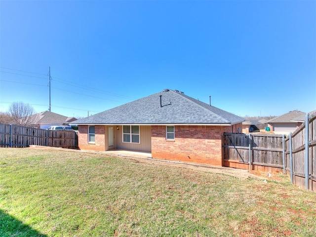 rear view of property with a yard, a fenced backyard, roof with shingles, and brick siding