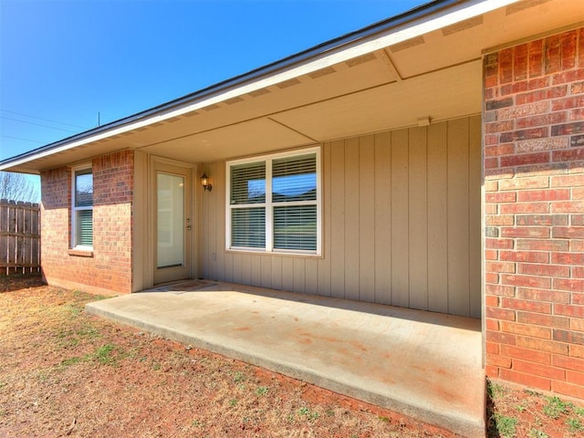 entrance to property with brick siding, fence, and a patio