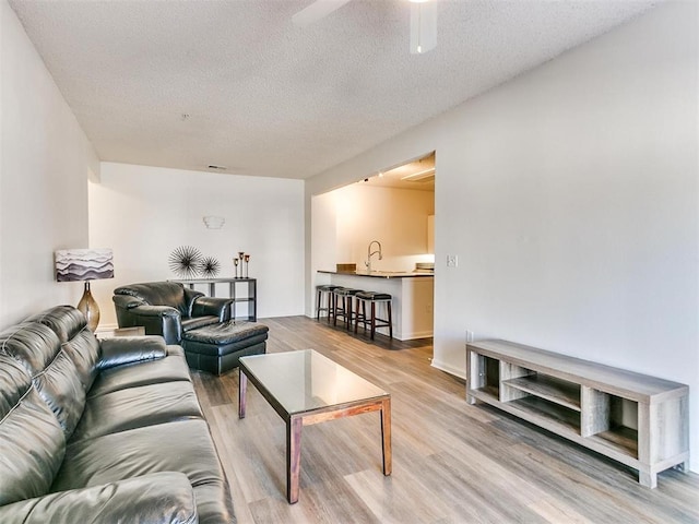 living area with a textured ceiling, ceiling fan, and light wood-style floors