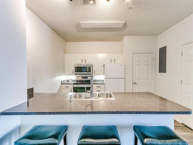 kitchen with stainless steel appliances, a peninsula, electric panel, dark countertops, and a kitchen bar