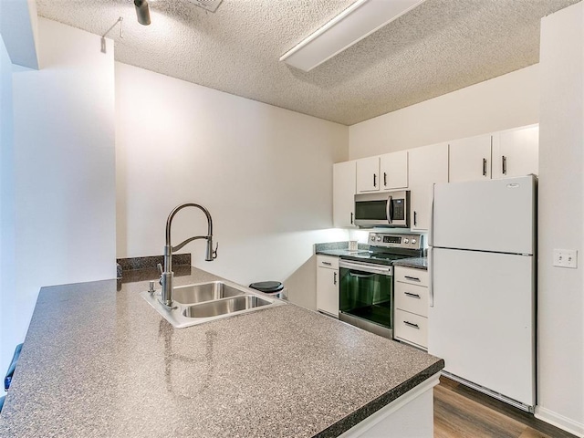 kitchen with a peninsula, wood finished floors, a sink, white cabinetry, and appliances with stainless steel finishes