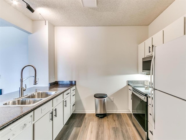 kitchen with white cabinets, appliances with stainless steel finishes, wood finished floors, a textured ceiling, and a sink