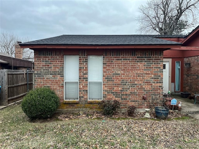 view of property exterior featuring brick siding, a shingled roof, and fence