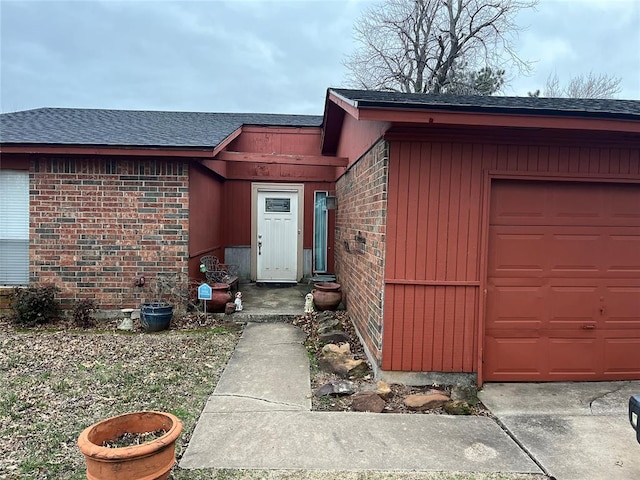 view of exterior entry featuring a shingled roof and brick siding