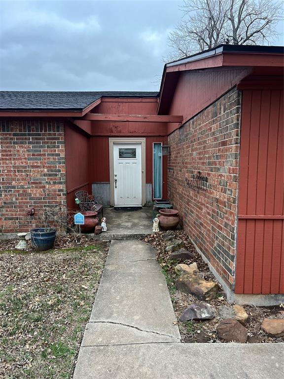 doorway to property with brick siding and roof with shingles