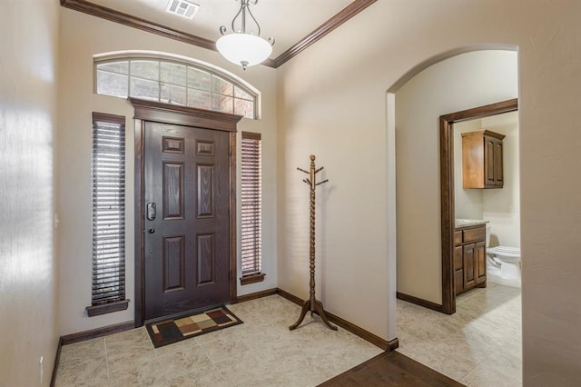 entryway featuring ornamental molding, arched walkways, visible vents, and baseboards