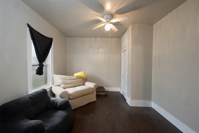 sitting room featuring ceiling fan, baseboards, dark wood-type flooring, and a textured wall