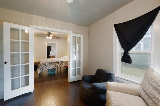 sitting room featuring dark wood-type flooring, french doors, a textured wall, and a ceiling fan