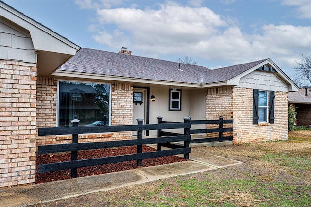 ranch-style house featuring a shingled roof, a chimney, brick siding, and a fenced front yard