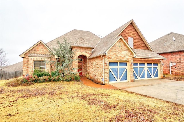 view of front of property with roof with shingles, brick siding, fence, a garage, and driveway