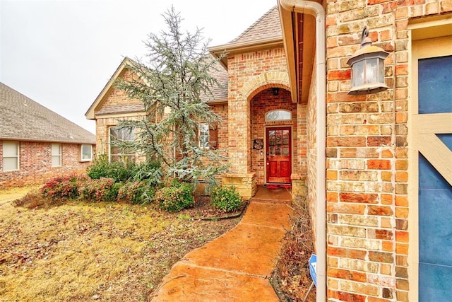 doorway to property with brick siding and a shingled roof