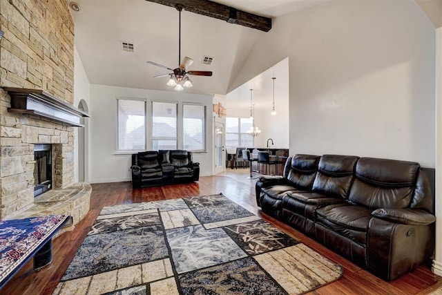 living room featuring a stone fireplace, wood finished floors, high vaulted ceiling, beamed ceiling, and ceiling fan with notable chandelier