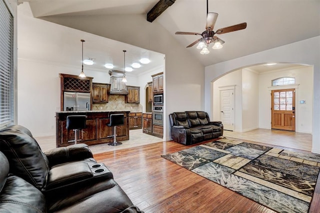 living room with arched walkways, light wood-style flooring, baseboards, beam ceiling, and crown molding