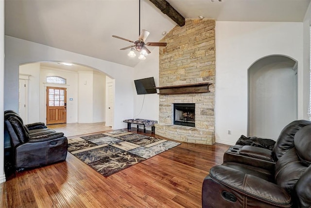 living room with arched walkways, beamed ceiling, wood finished floors, a stone fireplace, and high vaulted ceiling