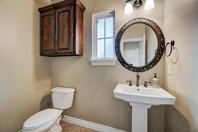 half bathroom featuring toilet, tile patterned flooring, baseboards, and a sink