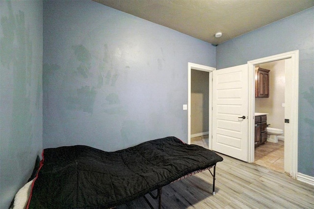 bedroom with connected bathroom and light wood-style flooring