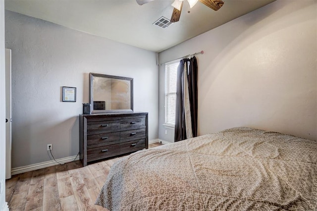 bedroom with a ceiling fan, visible vents, baseboards, and wood finished floors