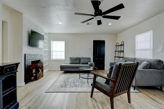 living area featuring a textured ceiling, light wood-style flooring, a fireplace, visible vents, and built in features