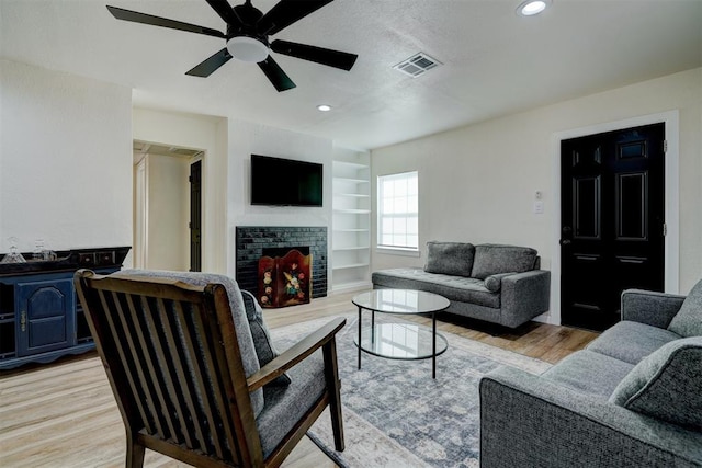 living area with light wood-type flooring, a fireplace, visible vents, and built in features