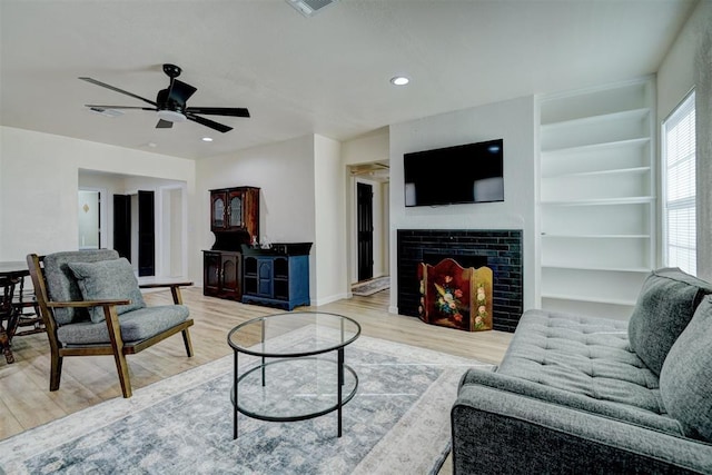 living area featuring built in shelves, recessed lighting, a fireplace, and wood finished floors