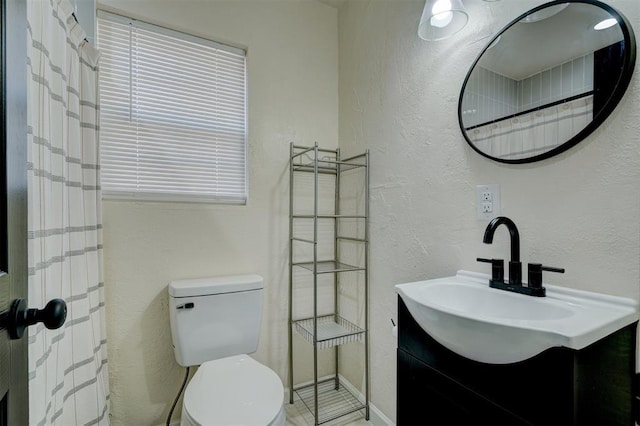 bathroom with toilet, vanity, baseboards, and a textured wall